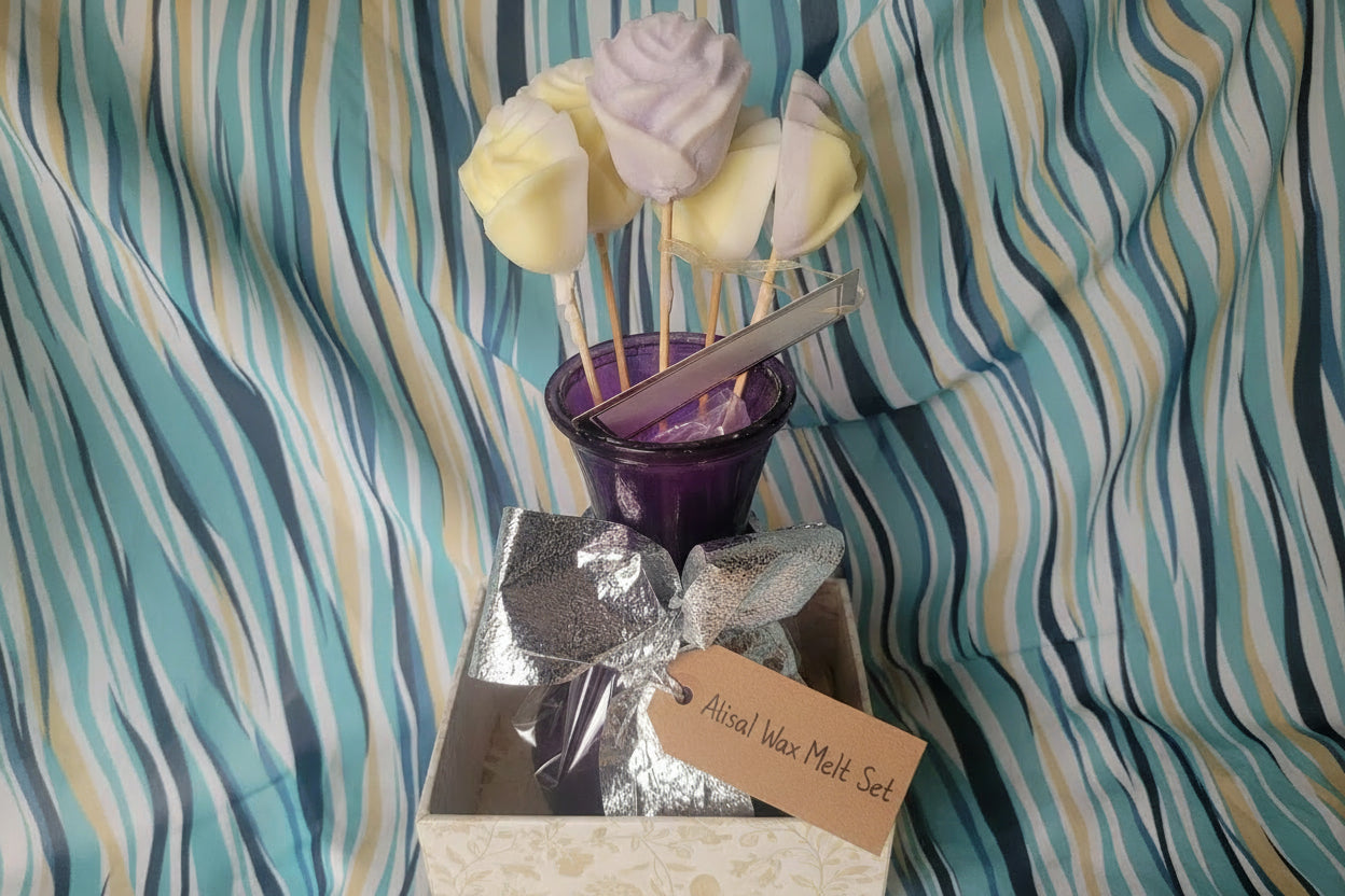 Decorative wax melts including a silver bow, purple container, and skewer with yellow and white decorative elements on a striped fabric background.